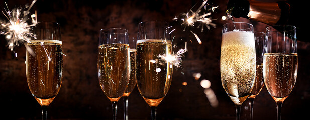 New year toasting with champagne and sparklers on dark background. Atmospheric close-up with champagne glasses for festive moments and space for text. - obrazy, fototapety, plakaty