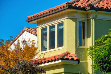 Light green stucco facade with red adobe roof tiles and neighboring white house with front yard...