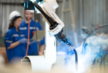Industrial engineer using laptop computer to control robotic welder arm operation in modern...