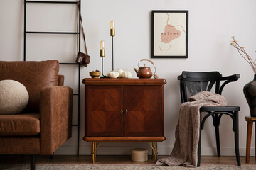 Warm and cozy living room interior with mock up poster frame with vintage sideboard, black chair, vase with dried flowers, patterned carpet, pumpkins, brown sofa and personal accessories. Template