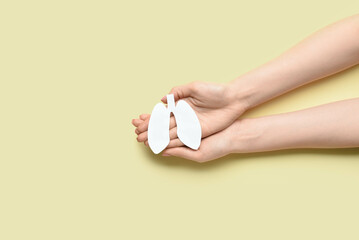 Female hands and white paper lungs on yellow background