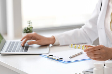 Female doctor with vitamins using laptop in clinic, closeup