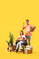 Young man with his wife in wheelchair, moving boxes and dog on yellow background