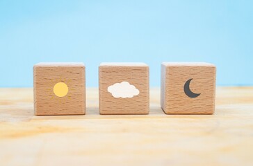 symbol of the meteorological the sun, the moon and the clouds represented in three wooden blocks on a blue background with copy space