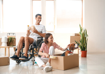 Fototapeta na wymiar Young woman with her husband in wheelchair and dog packing things in room on moving day