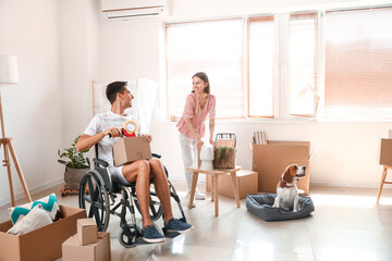 Young woman with her husband in wheelchair and dog packing things in room on moving day