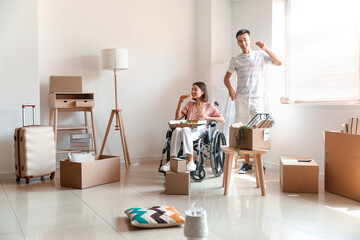 Young man and his wife in wheelchair eating pizza in room on moving day