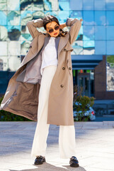 Portrait of a young beautiful brunette woman in gray coat and white trousers