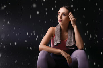 Sporty young woman with towel and dripping water on dark background