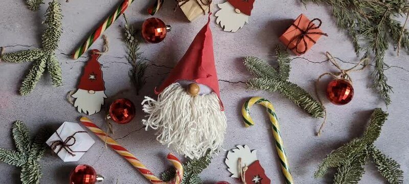 Christmas layout with Scandinavian gnome, Christmas tree toys, ornaments, balls, candy cane, gift boxes, fir branches and juniper branches on rustic white cracked table. Top view on the new year decor