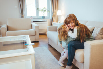Smiling single young mum embracing little preschool daughter with toy, playing in living room at...