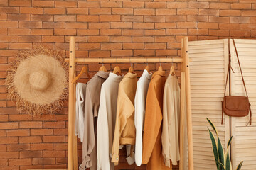 Fototapeta na wymiar Rack with stylish clothes and folding screen near brick wall