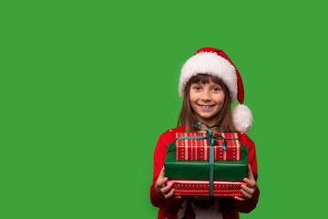 A little smiling girl in a Santa hat is holding a lot of gift boxes. New Year's gifts for Christmas. 2023. Isolated on a green background