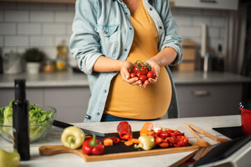 Young woman in kitchen. Beautiful pregnant woman making salad