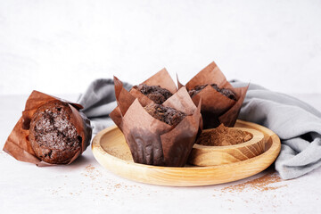 Wooden plate with tasty chocolate muffins and cocoa powder on light background