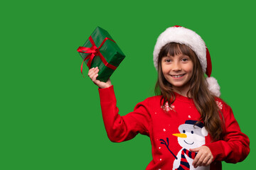 A smiling little girl in a Santa hat shows a beautifully wrapped present. Merry Christmas and Happy New Year 2023. Portrait isolated on green background