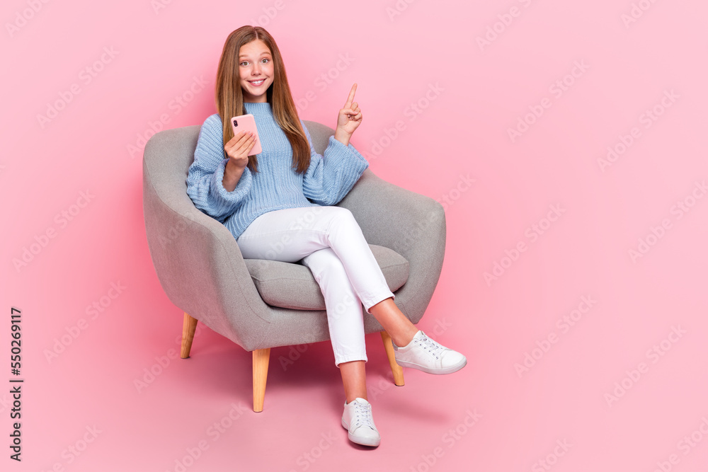 Poster Full body photo of funky teenager schoolkid girl sit sofa relax smartphone finger direct copyspace follow media isolated on pink color background