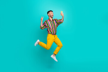 Plakat Full body photo of funny jumping air guy wear striped shirt showing v-sign selfie with smartphone hello followers isolated on cyan color background