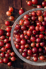 Ripe red gooseberry berries in a glass plate on a wooden table in the sun. View from above. Selective focus. Fresh summer vitamin harvest. Homegrown organic eco food 