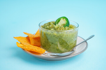 Plate with bowl of tasty green salsa sauce and nachos on color background