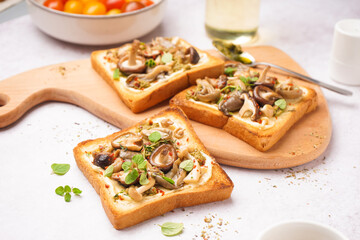 Wooden board of tasty toasts with cream cheese, mushrooms and pesto sauce on light background