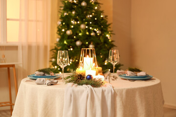 Christmas table setting with burning candles and fir branches in dining room