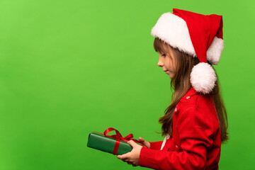 A little girl in a Santa hat holds a Christmas present in her hand, looks and will open it.