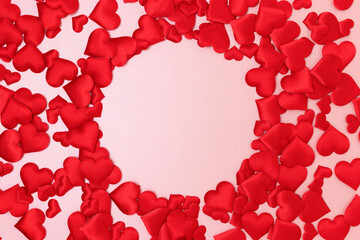 Round frame made of textile red confetti in a heart shape on a pink glittering background.