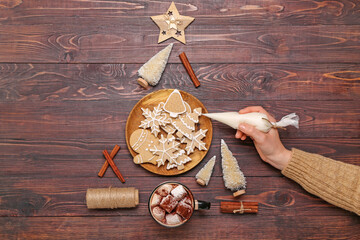 Female hand with bag of cream, Christmas cookies and decorations on wooden background