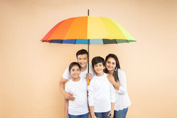 Happy indian family standing under big colorful umbrella against beige background. parents and...