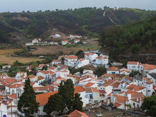 Fototapeta premium Aerial view over the town Odeceixe,white houses traditional village surrounded by Rio Seixe river, green hills and fields with grazing cows. Alentejo, Portugal.