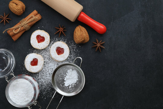 Cookies with strawberry jam powdered with powdered sugar, spices, powdered sugar in a jar, rolling pin, colander on dark background