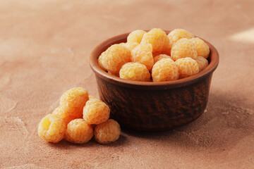 Composition of ripe yellow raspberries in a bowl on a marble background