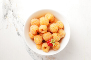 Ripe yellow raspberries in a bowl with a tea towel on a marble background. A bowl full of raspberries. Dessert ingredients.