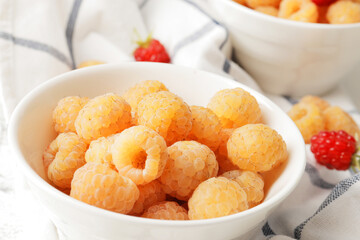Ripe yellow raspberries in a bowl with a tea towel on a marble background. A bowl full of raspberries. Dessert ingredients.