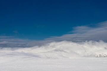 Fototapeta premium Snow-covered mountain range. Clouds over the mountain ridge. Winter mountain landscape.