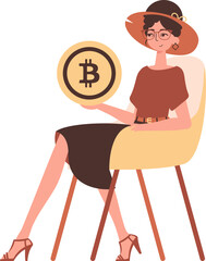 A woman sits in a chair and holds a bitcoin coin in her hands.
