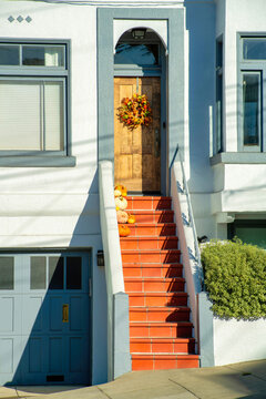Orange or red stairs with steep steps leading up to wooden front door with holiday reath and white stucco building exterior