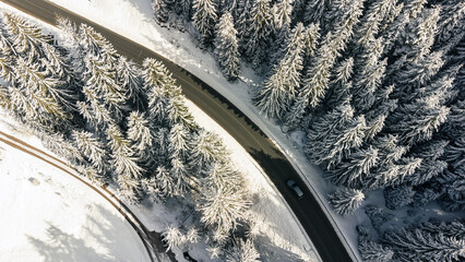 Car driving on winter mountain road. Aerial view of snowy forest with road.