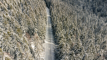 Aerial view of snowy forest with winter mountain road.