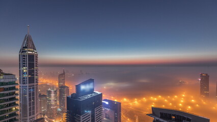 Naklejka premium Rare early morning winter fog above the Dubai Marina skyline and skyscrapers lighted by street lights aerial night to day timelapse.