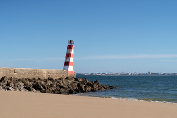 Lighthouse on a rock pier at the beach painted in red and white. Blue ocean and sky