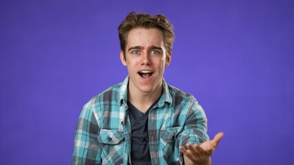 Portrait of amazed young man 20s shocked, saying WOW. Handsome guy surprised isolated on solid purple background.