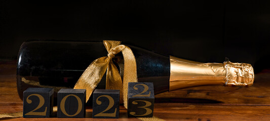 New Year 2022 / 2023 Sylvester New Year's Eve celebration holiday greeting card banner - Black cubes with year on sparkling wine or champagne bottle on table and black background