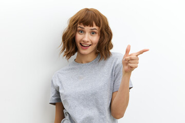 a happy, joyful woman with red hair color and beautiful styling looks smiling, pointing her finger at an empty space.