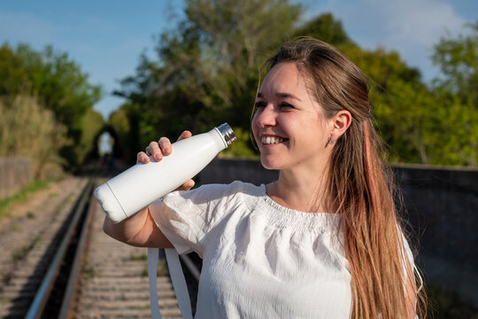 Mujer tomando líquido de botella metálica en blanco, para anuncios o propagandas. Fotografía con enfoque selectivo en la botella