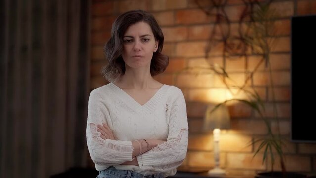 A frustrated and disappointed young woman with her arms crossed on her chest looks accusingly and suspiciously at the camera with a look demanding an apology. Social family relations.