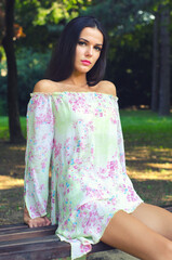 Portrait of the beautiful fashionable girl sitting on the bench in the park on sunny spring day