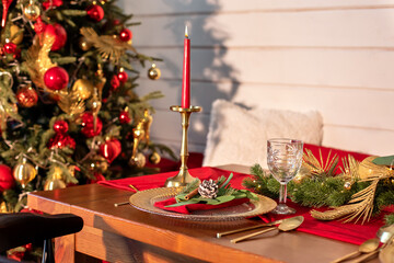 Festive table setting for Christmas dinner at home. Holiday Served table with decorations, candles and garland. Beautiful table setting with Christmas decorations and dishware in living room.	