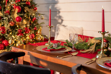 Festive table setting for Christmas dinner at home. Holiday Served table with decorations, candles and garland. Beautiful table setting with Christmas decorations and dishware in living room.	
